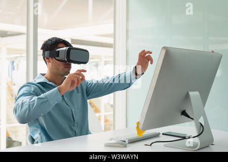 Male executive using virtual reality headset at desk Stock Photo