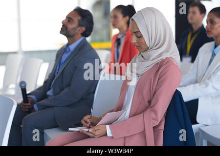 Businesswoman in hijab writing on notepad in a business seminar Stock Photo