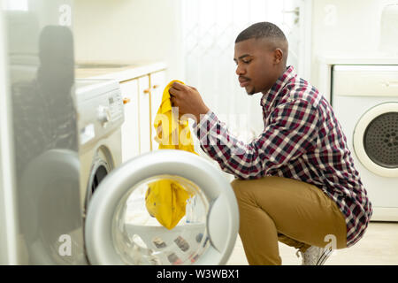 Man putting clothes in washing machine in kitchen at home Stock Photo