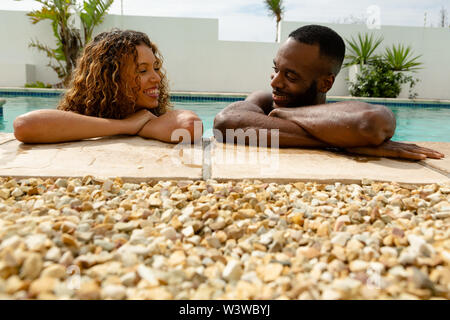 Couple leaning on the edge of a swimming pool and looking each other Stock Photo