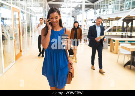 Businesswoman talking on mobile phone while walking in corridor at office Stock Photo
