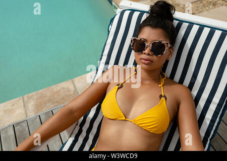 Woman in bikini relaxing on a sun lounger near swimming pool Stock Photo