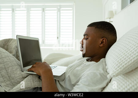 Man using laptop while lying on bed in bedroom at comfortable home Stock Photo