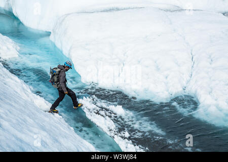 Young man in ice climbing gear stepping over a water filled crevasse on the Matanuska Glacier in Alaska. Stock Photo