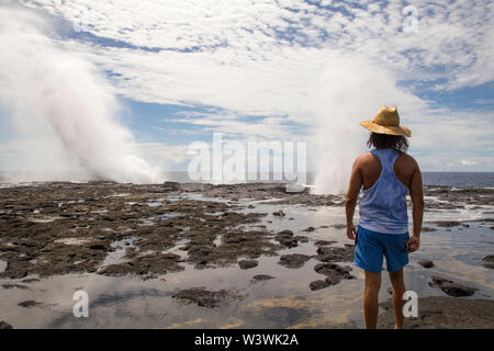 Man wearing blue singlet and shorts, staring at blowholes and ocean Stock Photo