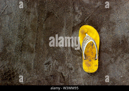 Only one dirty yellow sandal on the black sand. Horor concept. Stock Photo