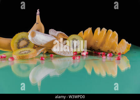 Delicious Hawaiian pineapple, banana, sliced green kiwi and red corn kernels on a green table and a black background - Nutritious and delicious snack Stock Photo