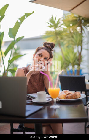 Beautiful student woman having breakfast on the terrace bread rolls with orange juice and espresso coffee - A laptop and a notebook on the black table Stock Photo