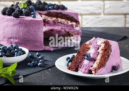 festive cake, blueberry and blackberry chocolate sponge cake layered with cream cheese on plates on a concrete table with brick wall at the background Stock Photo