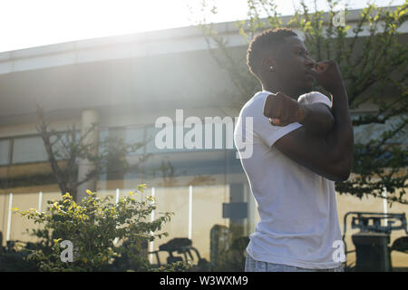 Portrait of African American man stretching arms in the city street. Young male fitness guy doing warm up in the morning Stock Photo