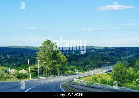 Asphalt road going through the forest on a sunny day. Bend in the road, clear blue sky with cirrus white clouds. Journey through Siberia Stock Photo