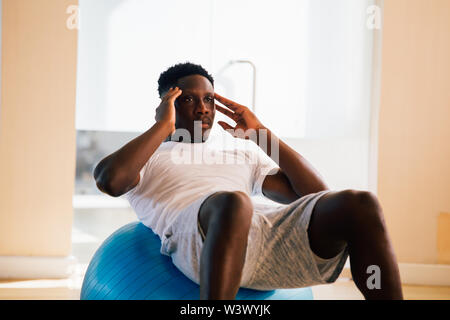 Young African American man doing sit-up exercise with swiss ball at gym. Male fitness model performing a crunch at fitness center Stock Photo