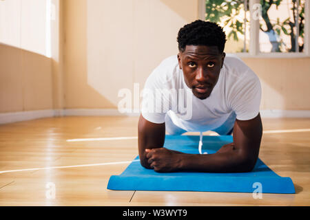 Young African American man doing a plank exercise at gym. Male fitness model with serous and determined face Stock Photo