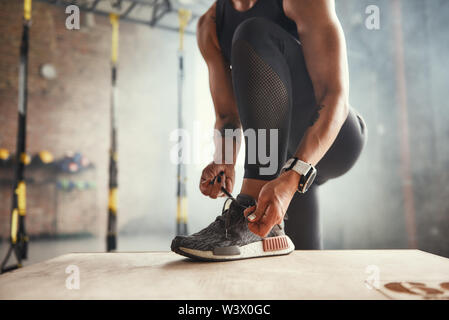 Preparing for workout. Cropped photo of beautiful young woman in sports clothing tying her shoelaces while exercising in gym. Professional sport. TRX Training. Healthy lifestyle Stock Photo