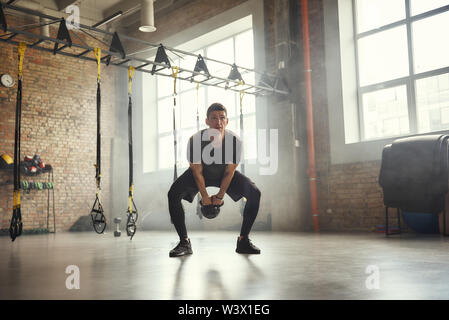 Weight exercise. Handsome and strong young man in sports clothing exercising with dumbbells while standing at gym. Bodybuilding concept. Workout. Healthy lifestyle Stock Photo