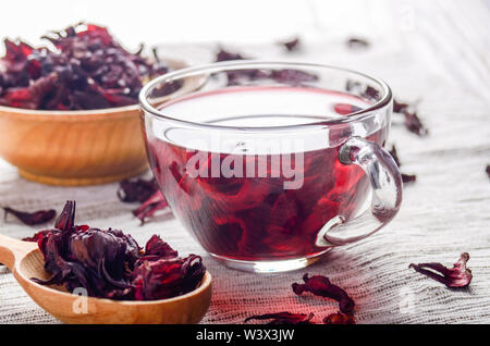 Closeup view at wooden bowl tea cup and spoon of dry hibiscus petals on linen cloth background Stock Photo