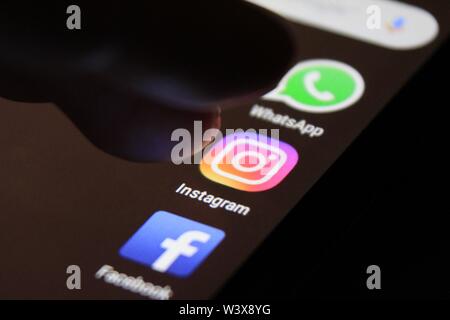 Alicante, Spain- July 6, 2019: Finger pressing Instagram icon on black mobile phone screen. Whatsapp and Facebook icons in the background. Stock Photo