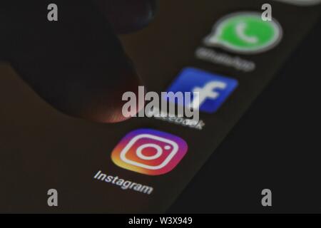 Alicante, Spain- July 6, 2019: Finger pressing Instagram icon on black mobile phone screen. Whatsapp and Facebook icons in the background. Stock Photo