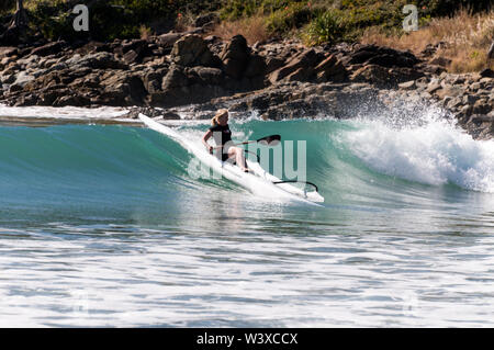 A young Australian woman riding the surf in her kayak in the Coral Sea at Agnes Water on the Queensland coast in Australia.   Agnes Water is a small Stock Photo