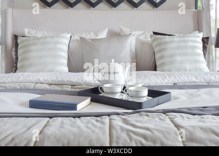 Decorative tray with book and tea set on the bed in modern bedroom Stock Photo