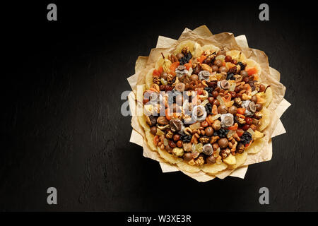 Decorative composition in the form of a bouquet of dried fruits and nuts on a black background Stock Photo