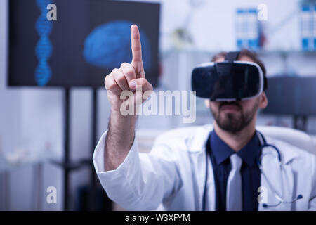 Male doctor in white coat wearing a virtual reality headset. Male doctor at hospital using virtual reality glasses. Stock Photo