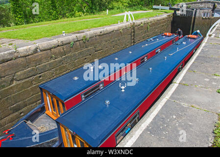 Two narrowboats traveling through a deep lock in English rural countryside scenery on British waterway canal Stock Photo