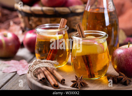 Two glasses of cider with sliced apples and cinnamon sticks on a wooden platter with basket of apples in background Stock Photo