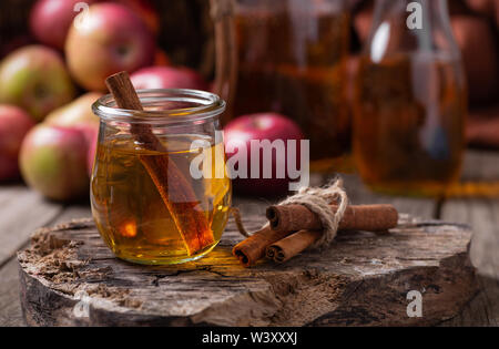 Glass of apple cider with cinnamon sticks on a rustic wood surface with red apples in background Stock Photo
