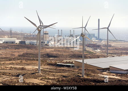 White turbines at wind farm with power station and sea in background, arid landscape on sunny summer day, sustainable renewable electricity concept Stock Photo