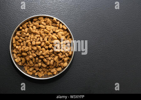 Bowl with dry food for domestic animals on black ceramic floor Stock Photo