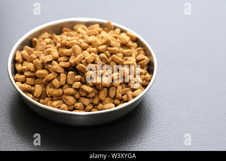 Bowl with dry food for domestic animals on black ceramic floor Stock Photo
