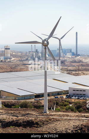 White turbines at wind farm with power station and sea in background, arid landscape on sunny summer day, sustainable renewable electricity concept Stock Photo