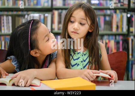 Two cute girls are jealous of each other while reading books in library while teacher teaching. People lifestyles and education. Young friendship and Stock Photo