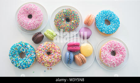 Donuts and french macarons on white table, close up view with details, top view