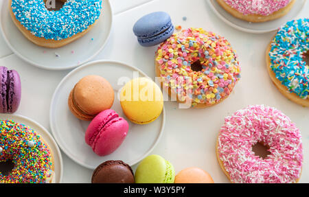 Donuts and french macarons on white table, close up view with details, top view