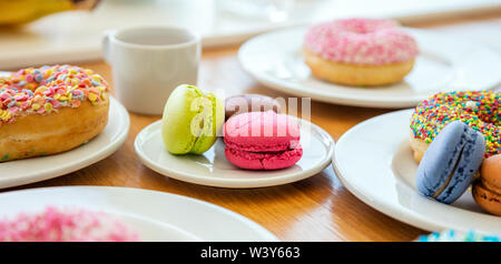 Donuts and french macarons on wooden table, close up view with details, banner.