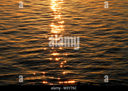 Texture of ripples on the water with bright sun highlights during sunset. Stock Photo