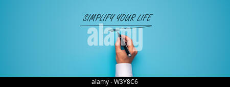 Male hand writing a Simplify your life sign with black marker over blue background. Stock Photo