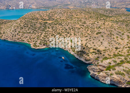 Aerial drone view of boats in clear, blue water next to a dry, yellow summer coastline (Crete, Greece) Stock Photo