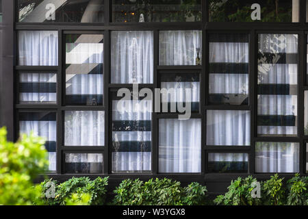 View of the modern windows and white curtain, the glass of which reflects the opposite fountain and garden. Abstract pattern background. Stock Photo