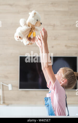 Beautiful little girl on sofa hugging teddy bear. The concept of a happy childhood, game in the family.