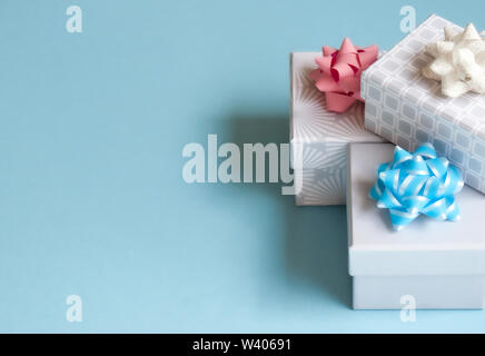 Three light gray gift boxes with light bow on blue background. Festive concept. Stock Photo