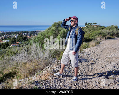 Traveler guy with a backpack behind his back, examining the neighborhood standing on a hill Stock Photo