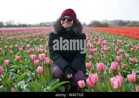 Young woman bundled up squatting in a tulip field. Stock Photo