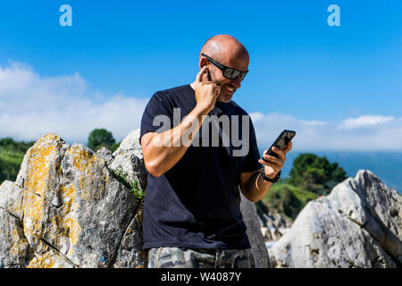 bald man on beach using headphones and mobile phone Stock Photo