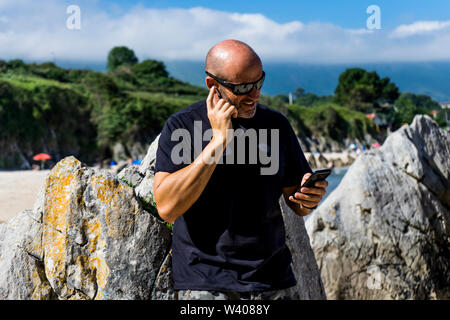 bald man on beach using headphones and mobile phone Stock Photo