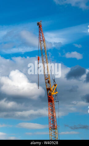 An orange tower crane against a blue sky with cumulonimbus clouds Stock Photo