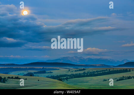 full moon setting above peaks of the flint creek range and foothills near avon, montana Stock Photo