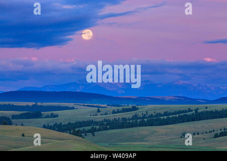 full moon setting above peaks of the flint creek range and foothills near avon, montana Stock Photo